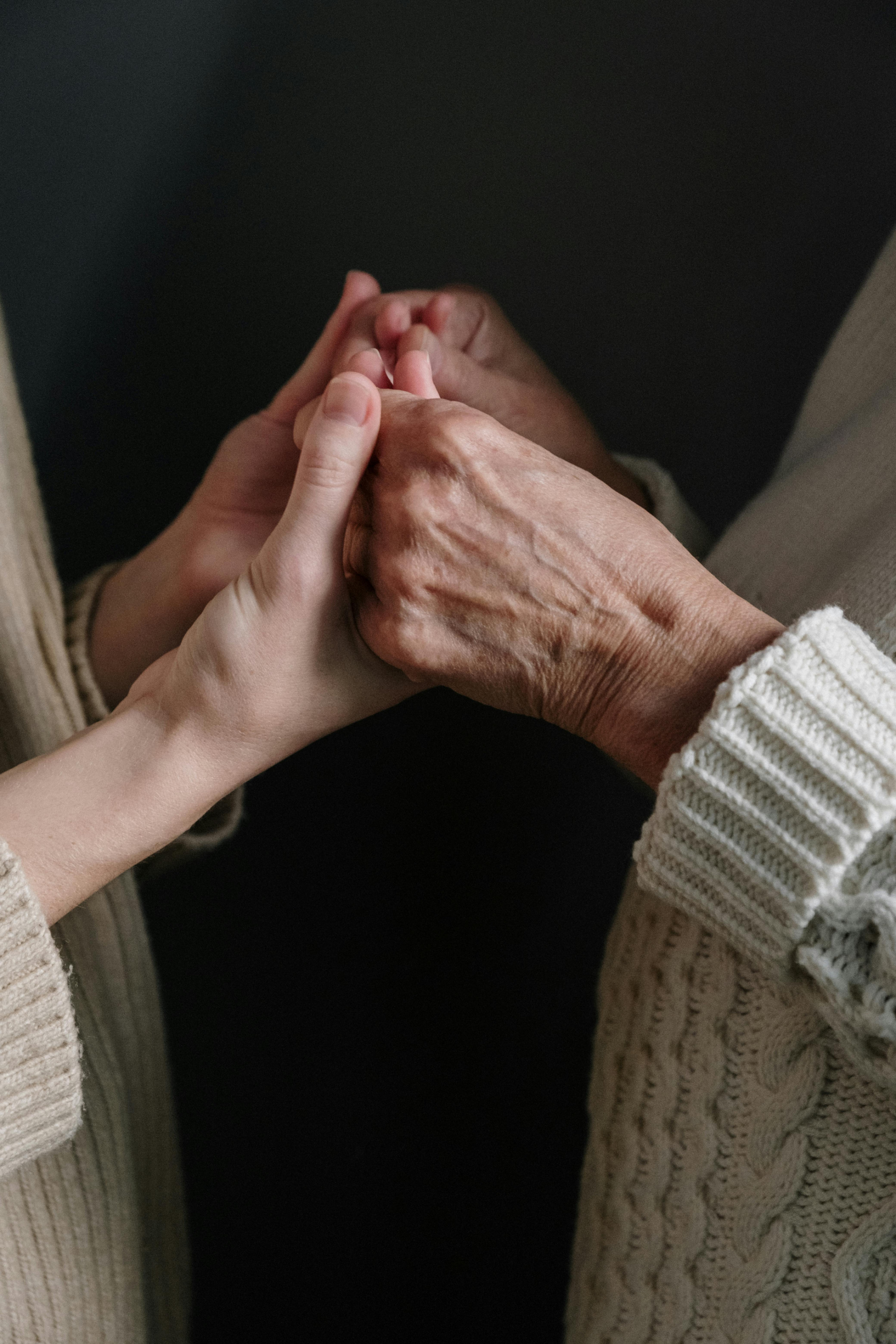 Eine jüngere Person hält die Hand einer älteren Person, als würde sie ihr helfen, das Gleichgewicht zu halten.
